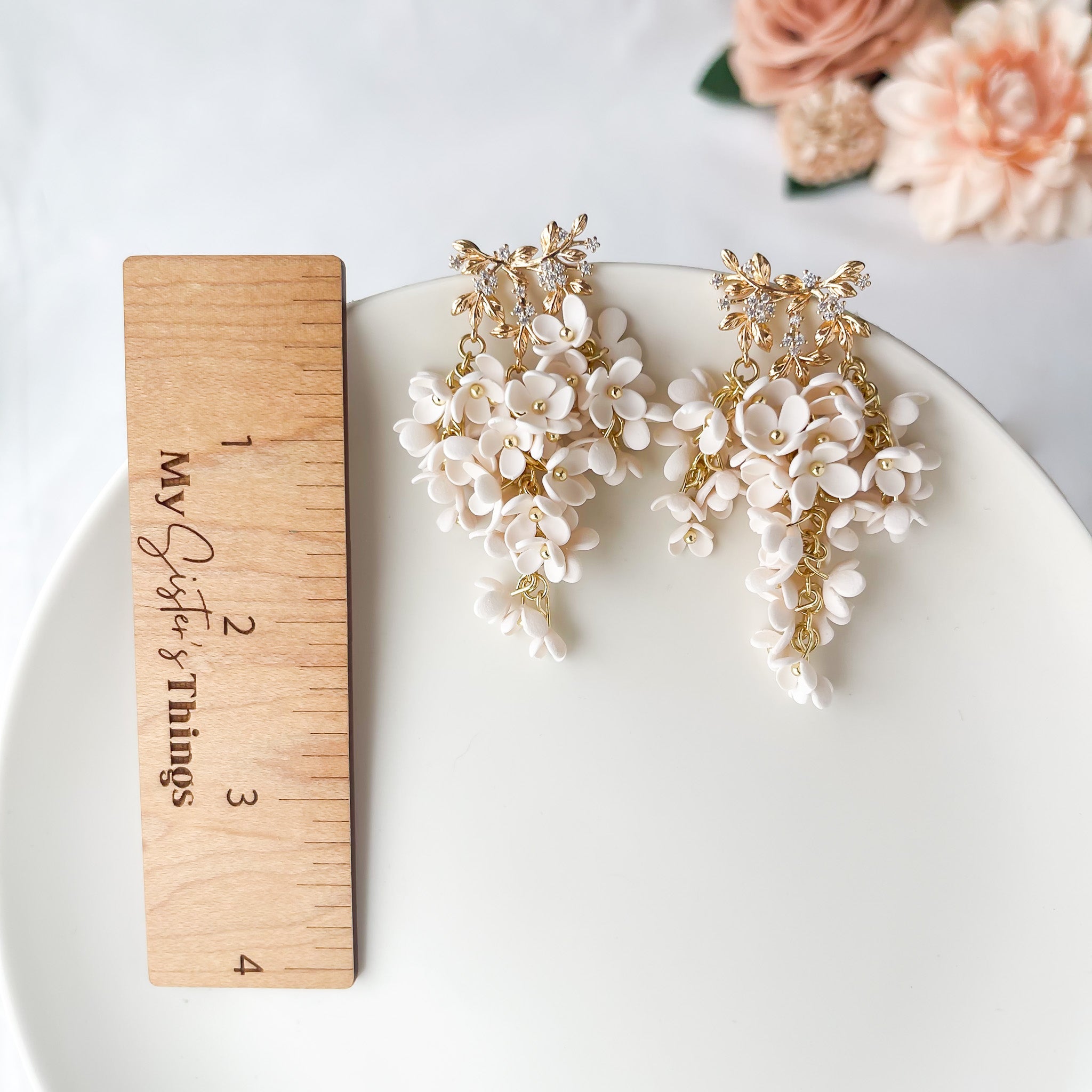 Floral earrings on a white plate with a wooden ruler for scale, against a light background.