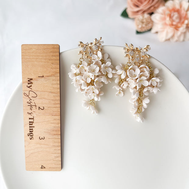 Floral earrings on a white plate with a wooden ruler for scale, against a light background.