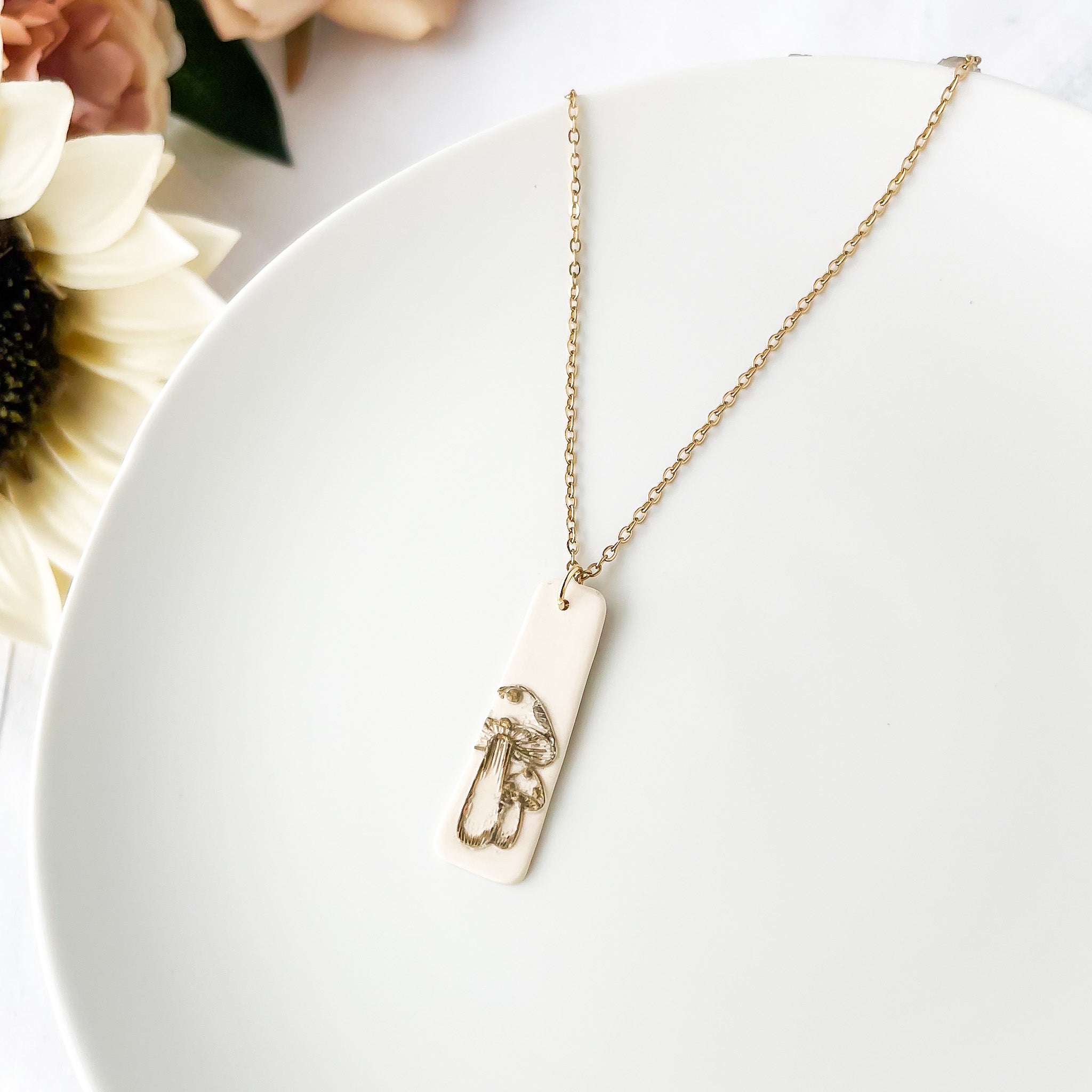 Necklace with a mushroom design pendant on a white surface with flowers in background