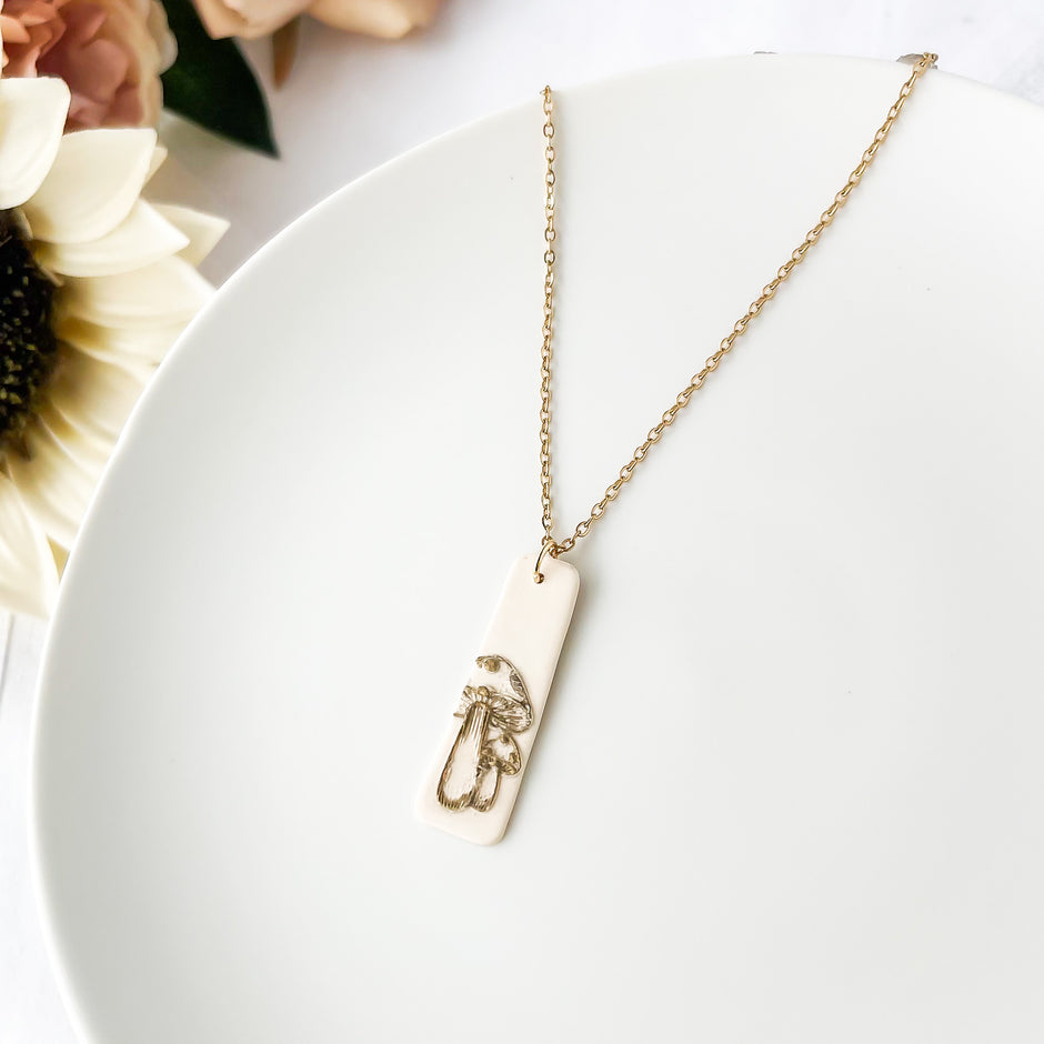 Necklace with a mushroom design pendant on a white surface with flowers in background