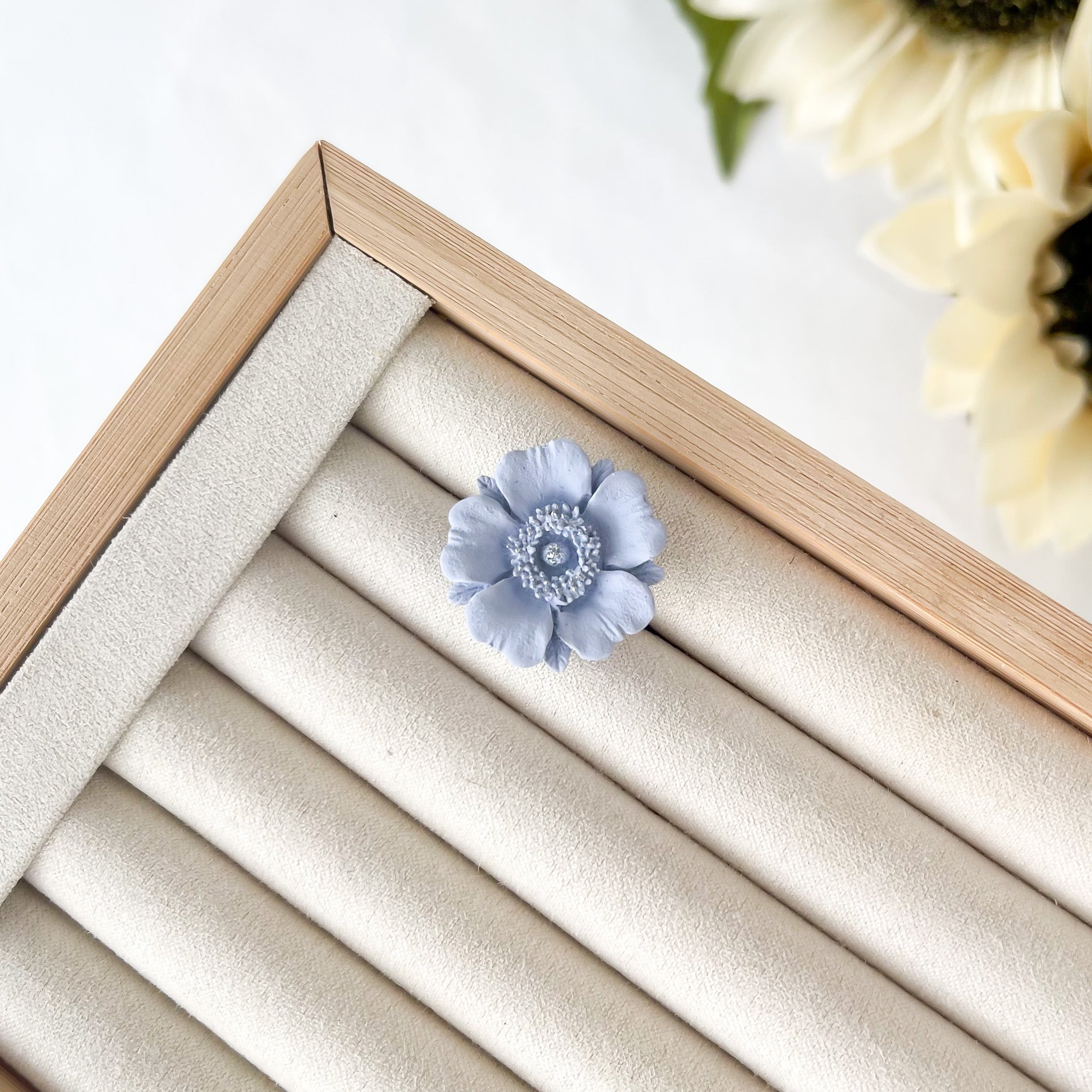 Blue flower-shaped object on a beige jewelry display box with a wooden frame.