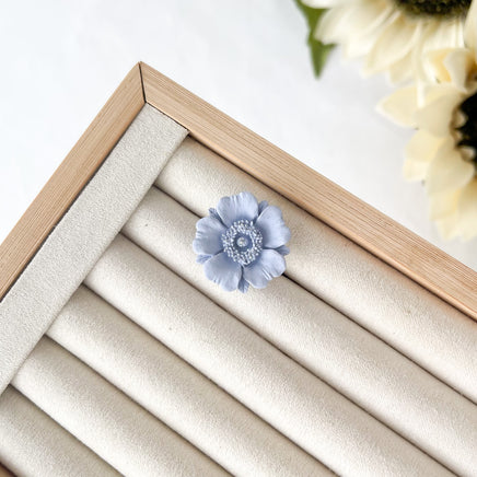 Blue flower-shaped object on a beige jewelry display box with a wooden frame.