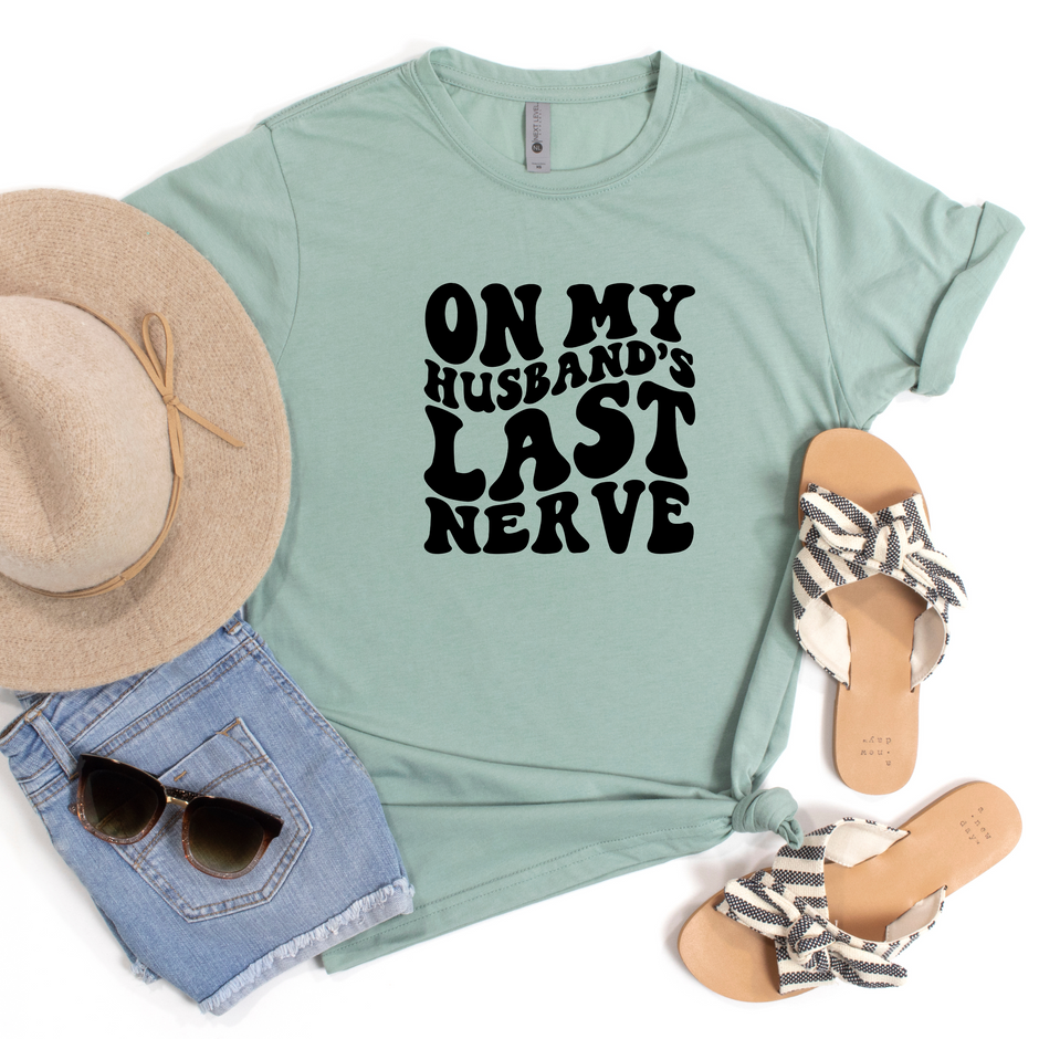 Light green-shirt with 'On My Husband's Last Nerve' text, paired with a hat, sunglasses, and sandals on a white background.