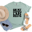 Light green-shirt with 'On My Husband's Last Nerve' text, paired with a hat, sunglasses, and sandals on a white background.
