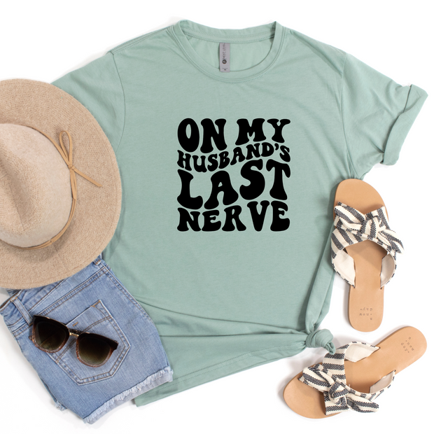 Light green-shirt with 'On My Husband's Last Nerve' text, paired with a hat, sunglasses, and sandals on a white background.