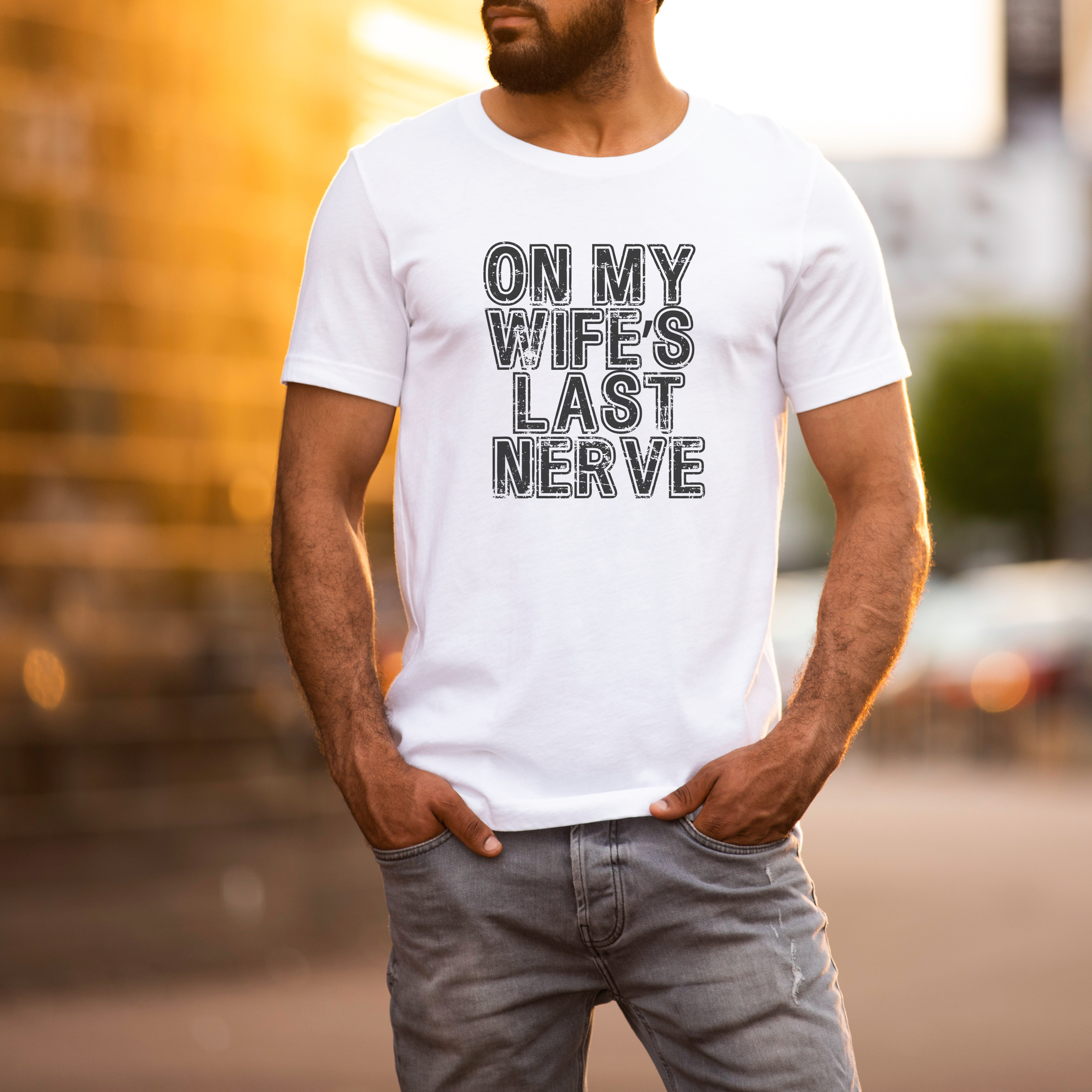 Man wearing a white t-shirt with text 'ON MY WIFE'S LAST NERVE' in an urban setting.