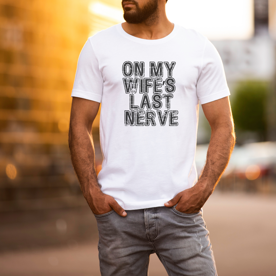 Man wearing a white t-shirt with text 'ON MY WIFE'S LAST NERVE' in an urban setting.