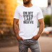 Man wearing a white t-shirt with text 'ON MY WIFE'S LAST NERVE' in an urban setting.