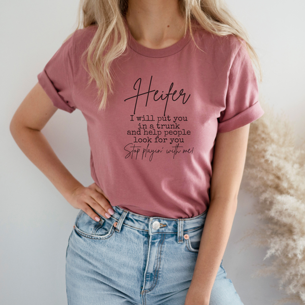 Person wearing a pink t-shirt with text and blue jeans against a neutral background