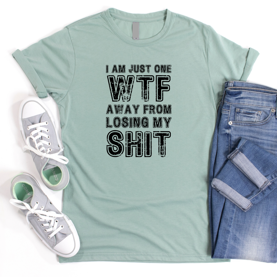 A green unisex t-shirt with the text 'I'm Just One WTF Away From Losing My Shit' printed on it, paired with blue denim jeans and white low-top sneakers.
