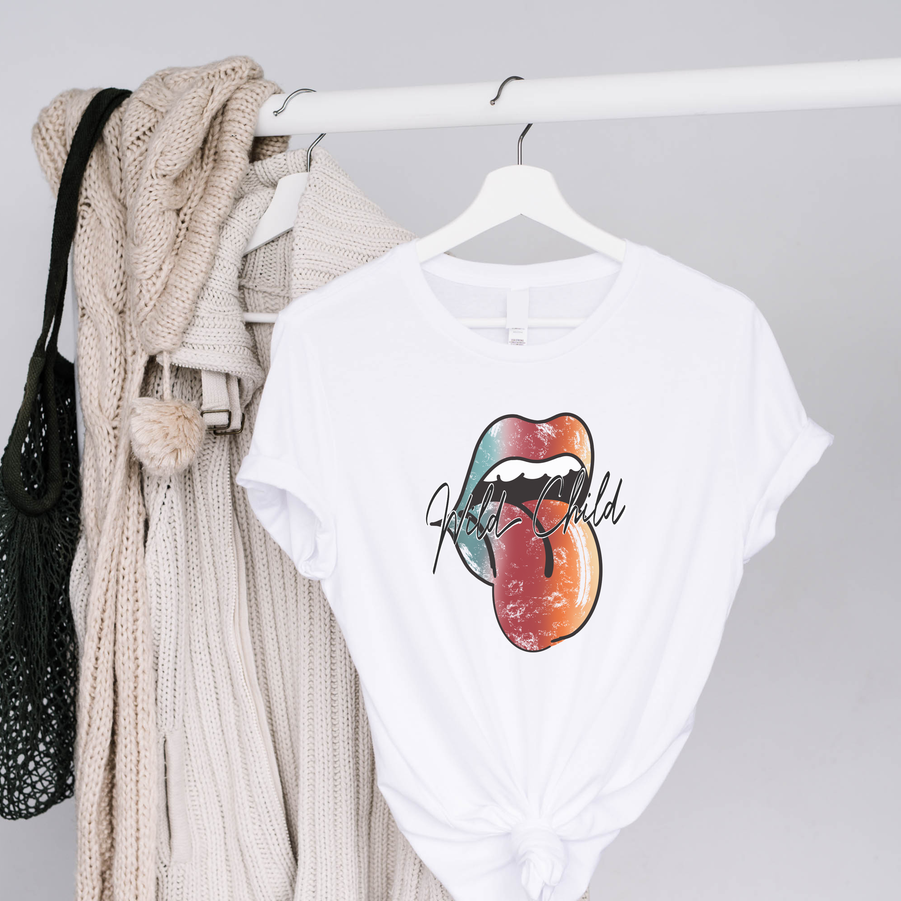 White t-shirt with colorful lips graphic and 'Wild Child' text on a hanger against a gray background.