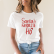 Person wearing a white t-shirt with 'Santa's Favorite Ho' text in red.