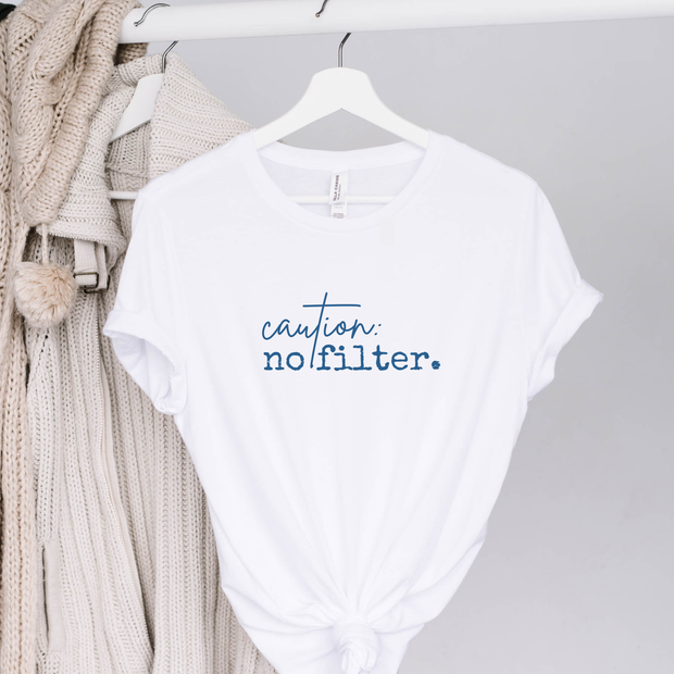 White t-shirt with 'caution: no filter.' text on a hanger among clothes.