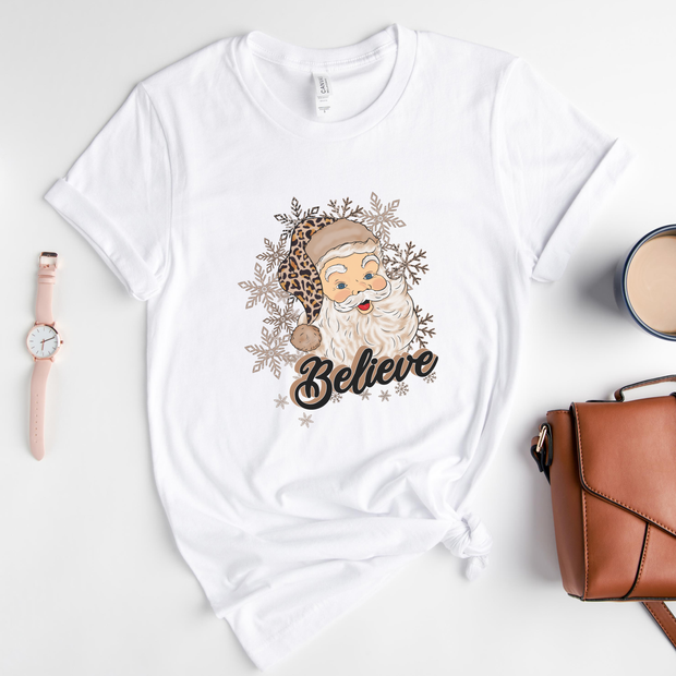 White t-shirt with Santa Claus graphic and 'Believe' text on a light gray background.